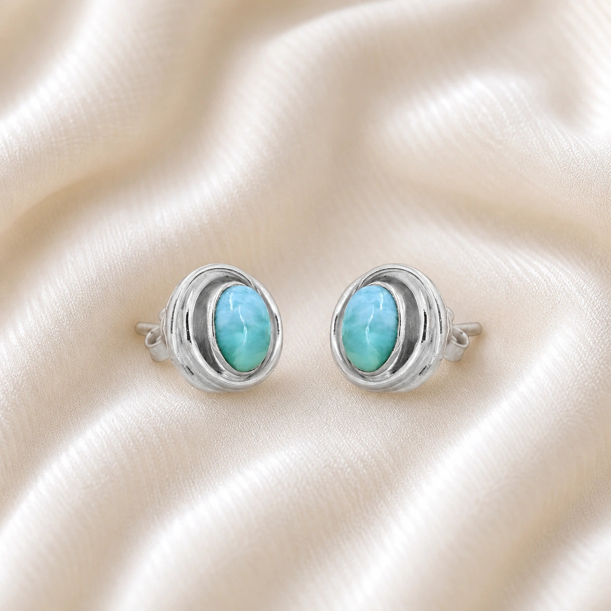 Larimar_earrings_sterling_silver_stud_design_with_oval_larimar_stone_shown_slightly_angled_on_soft_fabric_background
