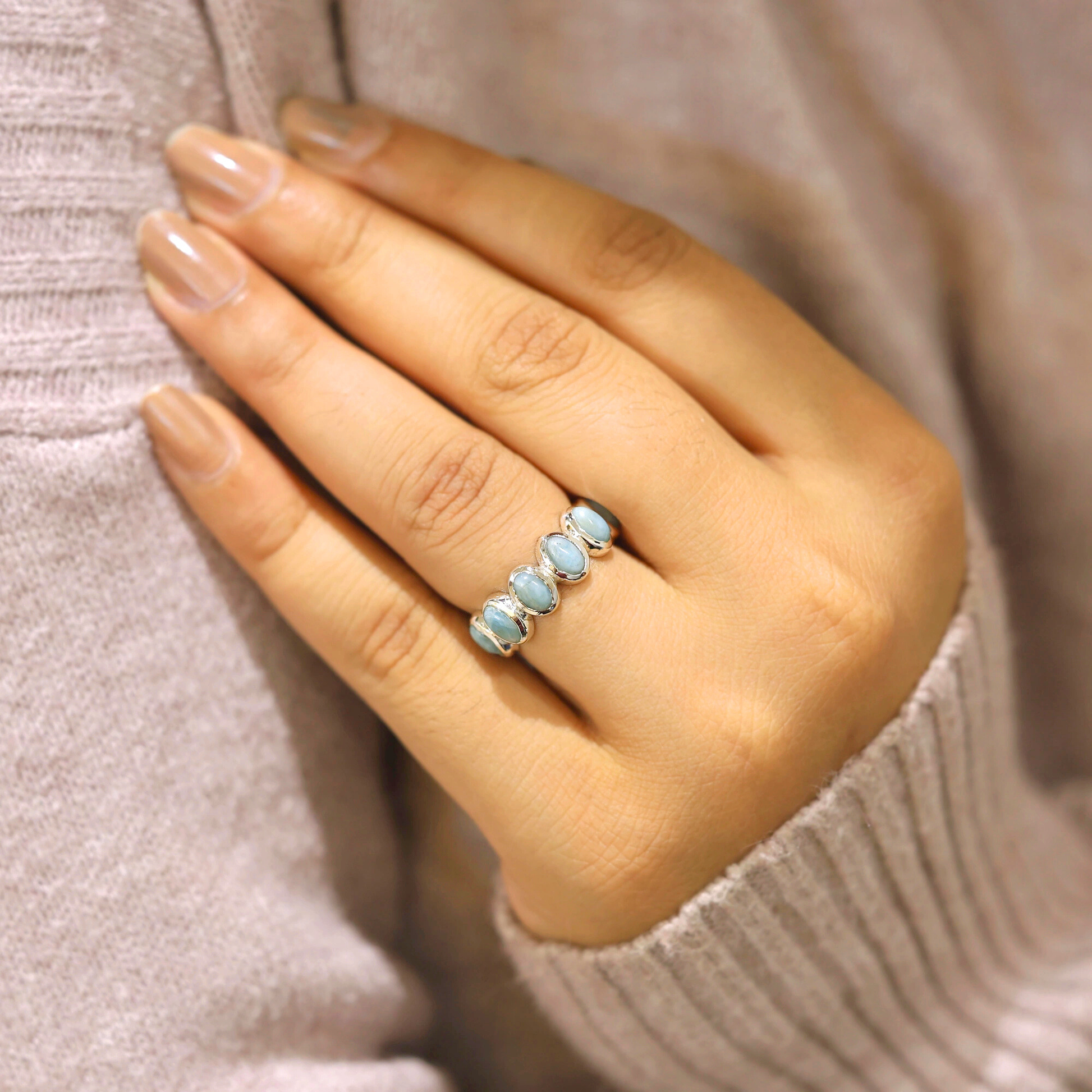 Silver larimar ring displaying five large oval pale blue stones prominently worn on a finger.