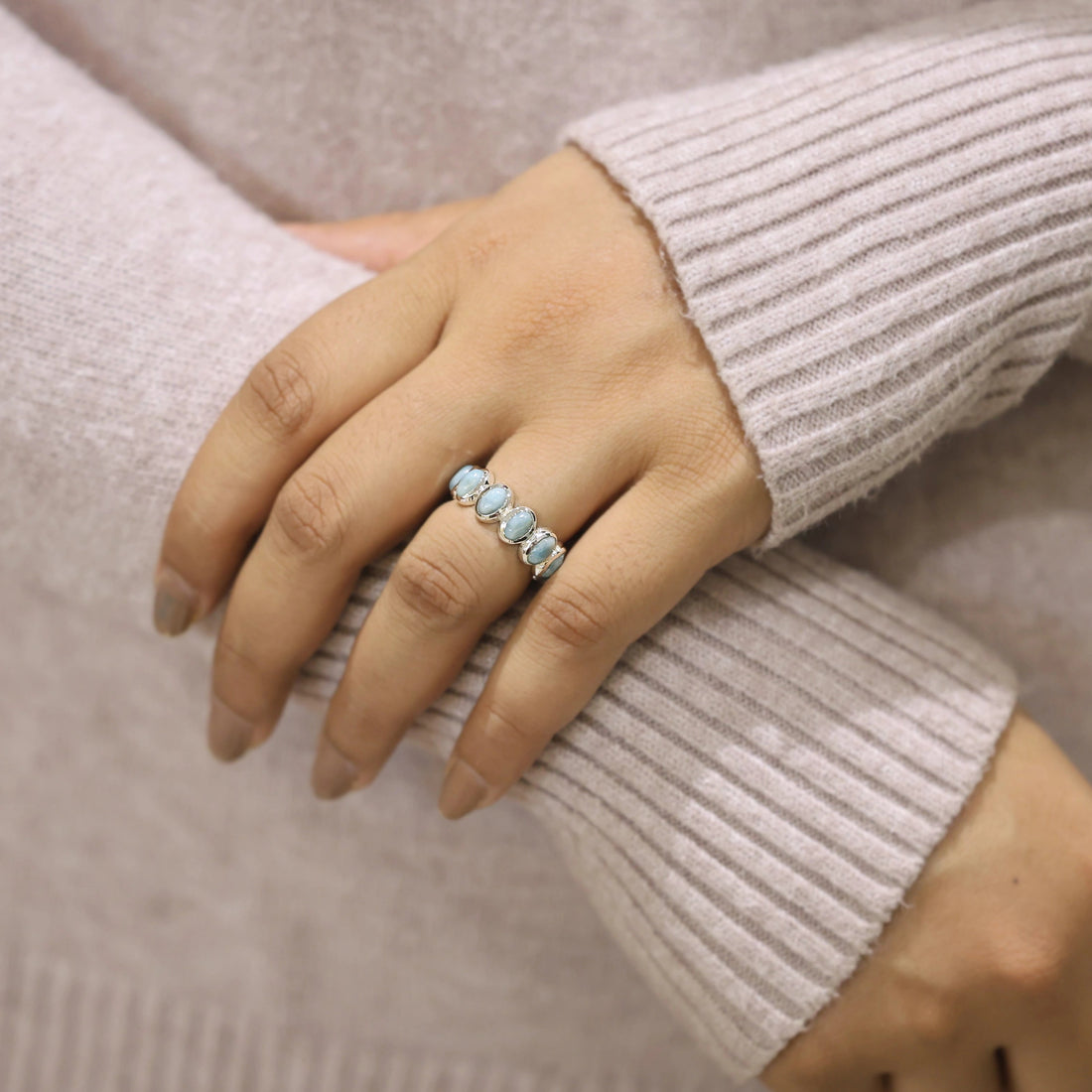 Silver Larimar eternity ring with oval blue stones standing upright on a softly draped creamy white velvet cloth.