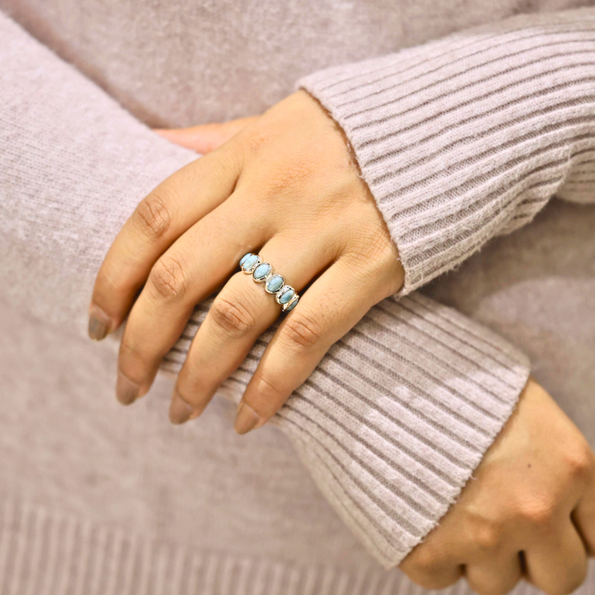 Silver larimar ring showing five bezel set oval stones worn on a finger against a sweater background.
