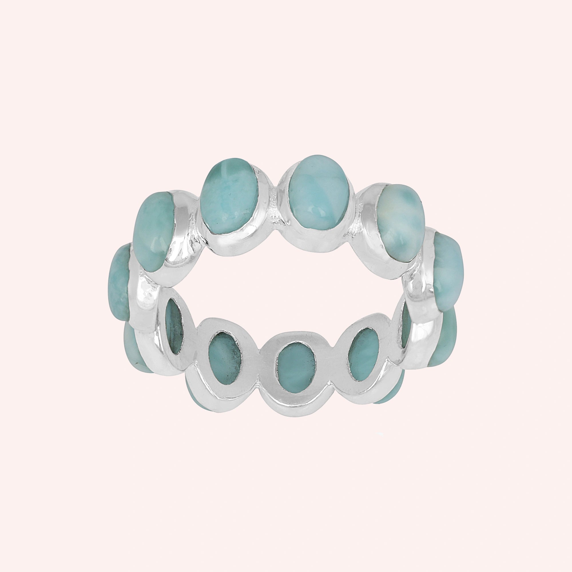 Silver larimar ring displaying numerous round pale blue stones in an eternity band on a light pink background.