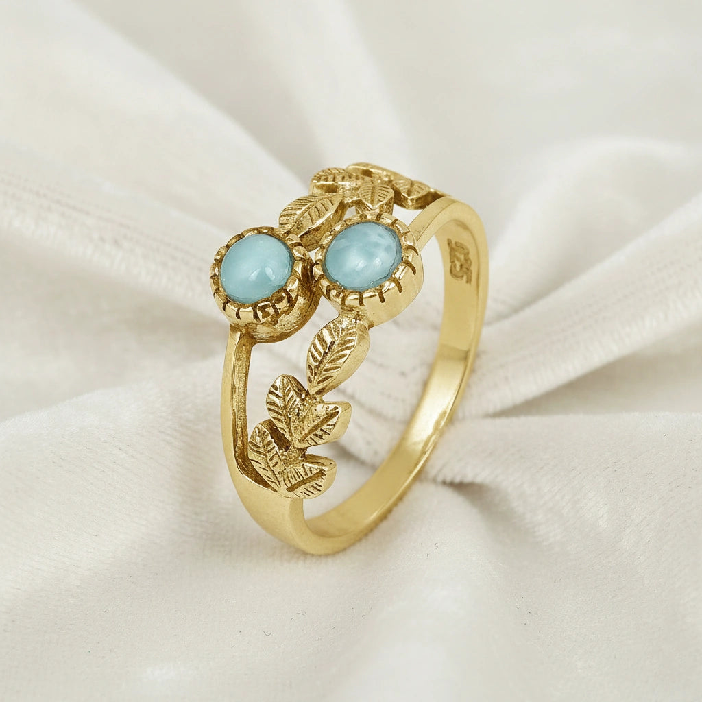 Gold plated sterling silver leaf ring with two larimar stones on white draped fabric from an elevated front angle