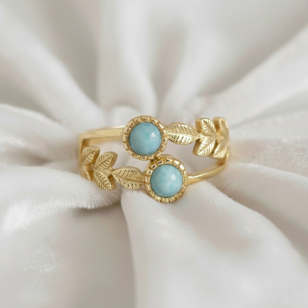 Gold plated sterling silver leaf ring with two larimar stones on an off white draped fabric from a low angle view