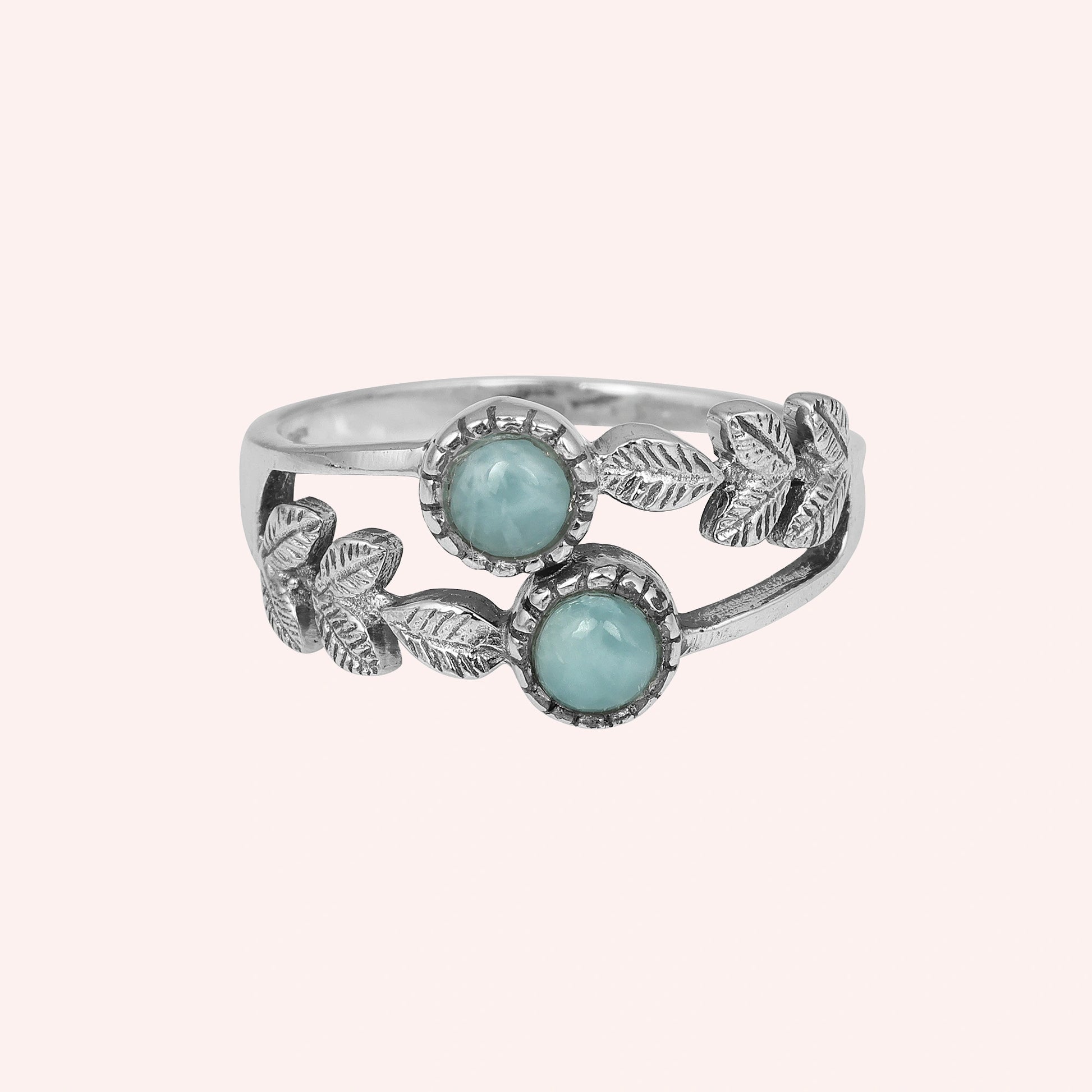 Studio shot of a sterling silver leaf ring with two round Larimar stones on a light pink solid background viewed straight on