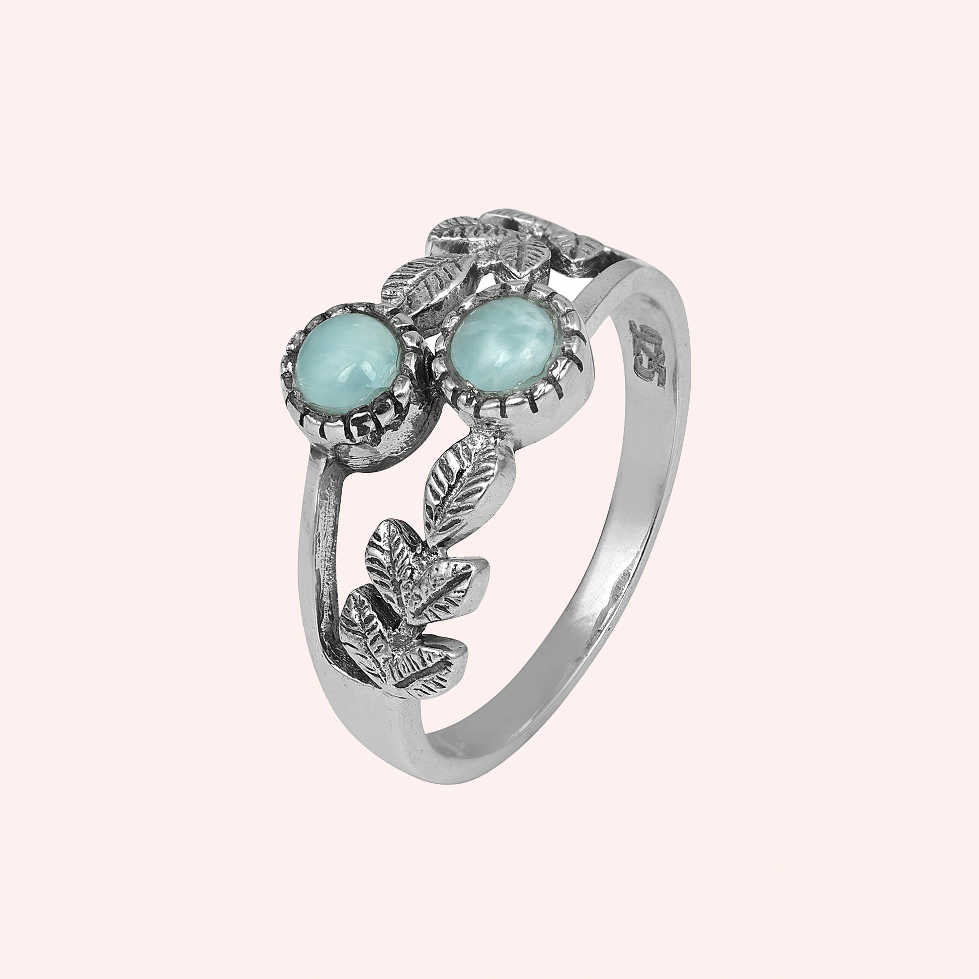 Detailed sterling silver leaf ring with two round Larimar stones on a light pink background viewed from an elevated front angle