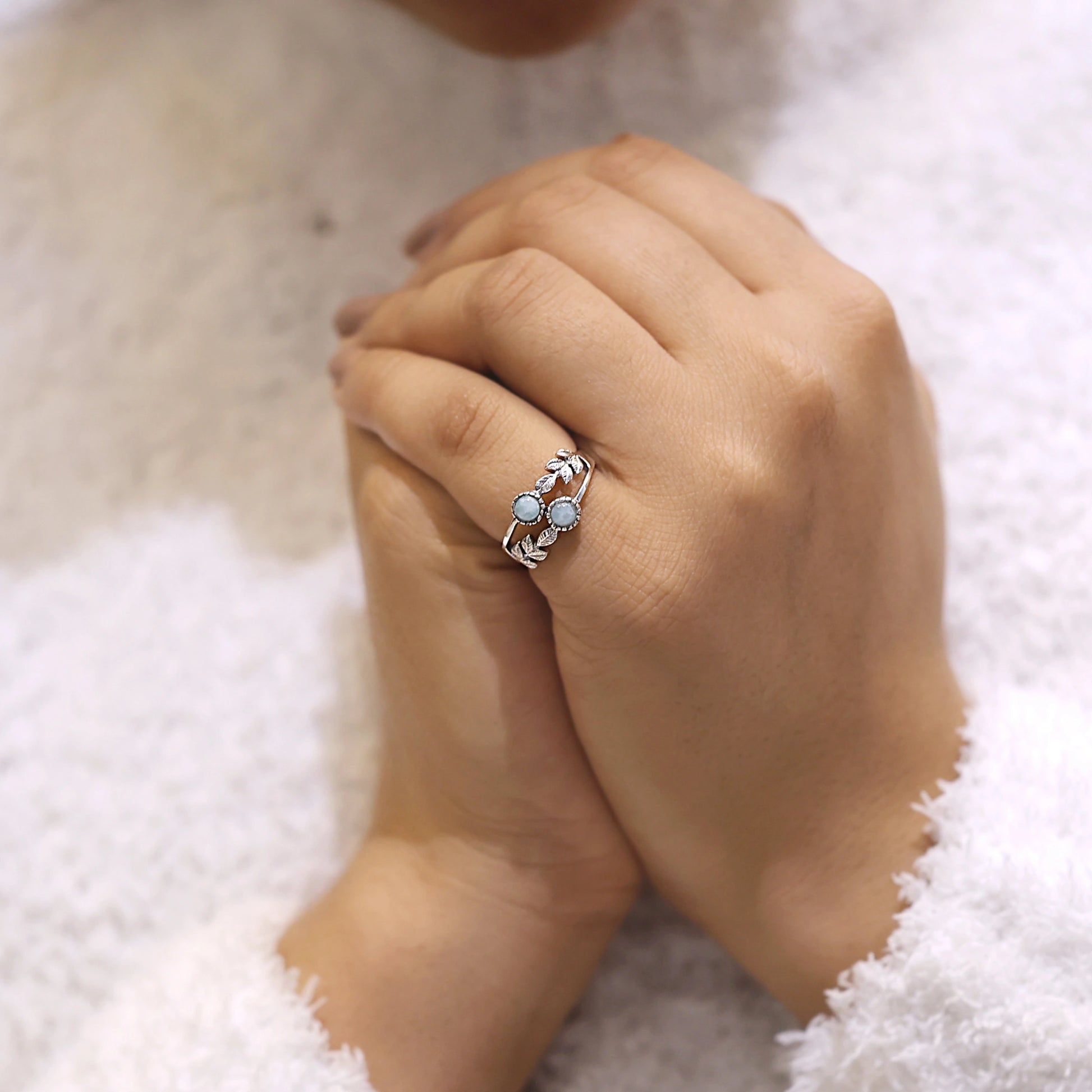 Close up of a sterling silver leaf ring with two round Larimar stones worn on a hand against a white background viewed straight on