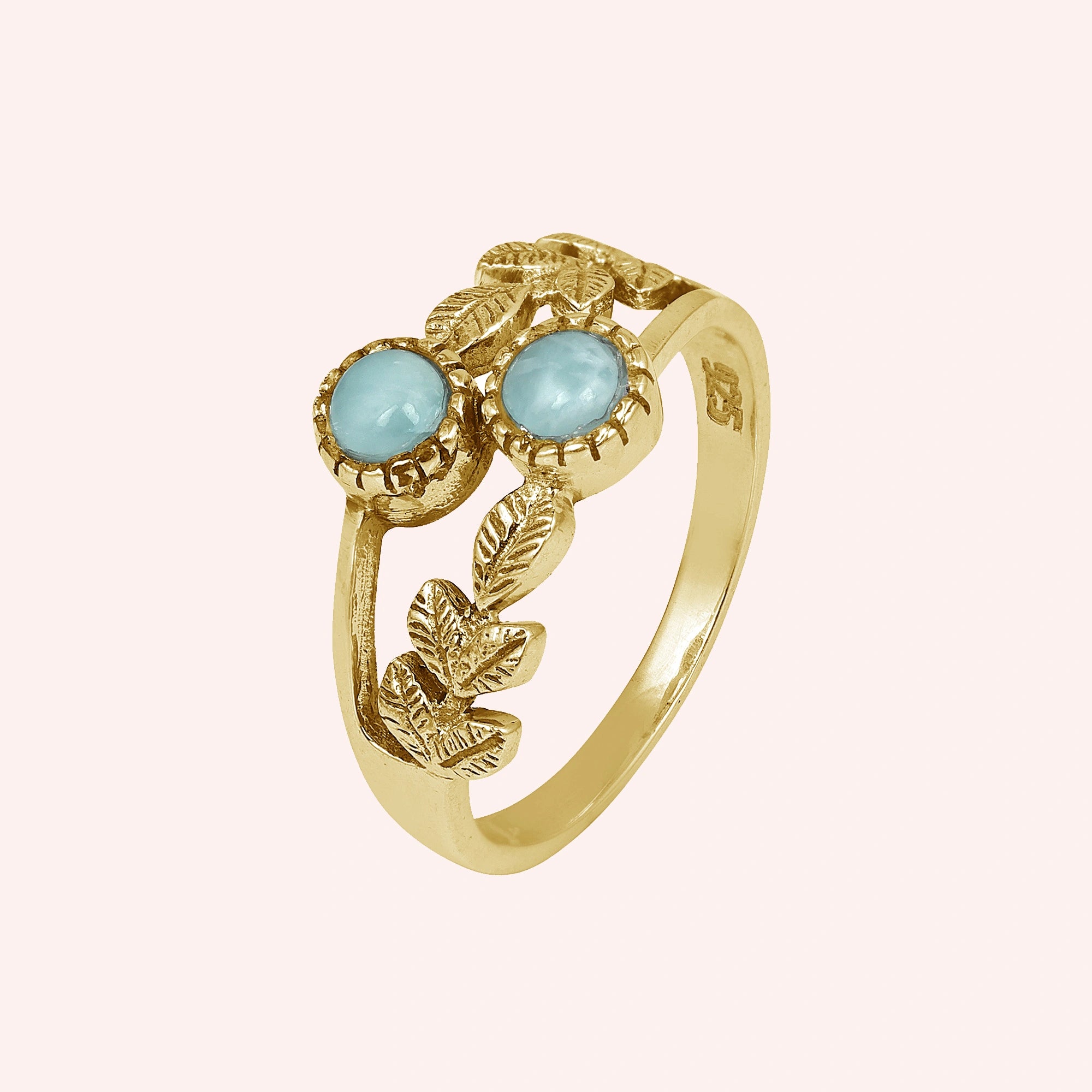Gold plated sterling silver leaf ring with two larimar stones on light pink background from an elevated front angle