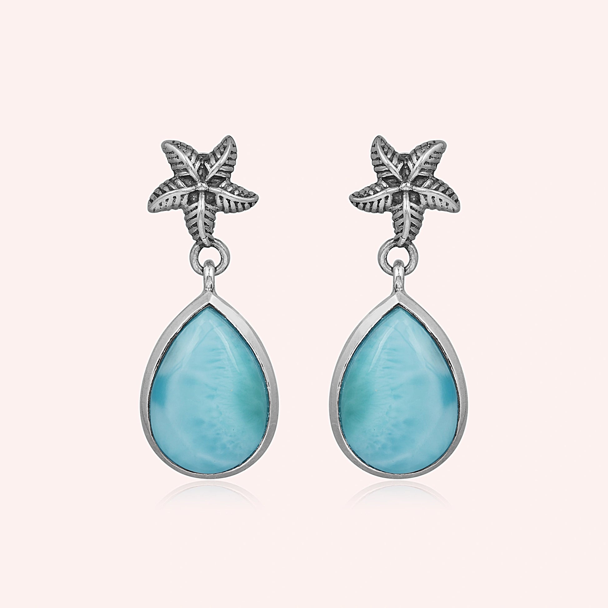 Starfish earrings with teardrop Larimar stones hang against a pink background studio shot slightly overhead view