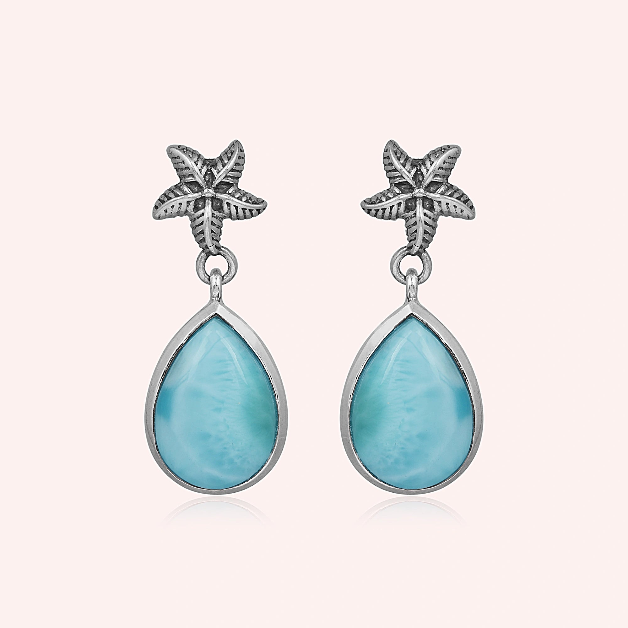 Starfish earrings with teardrop Larimar stones hang against a pink background studio shot slightly overhead view
