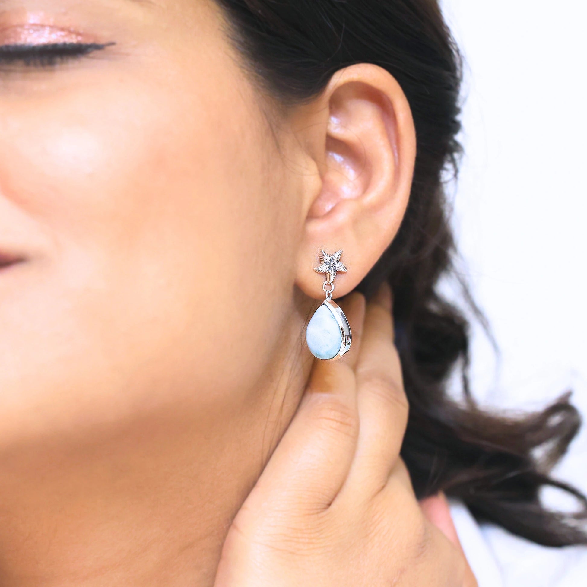 Sterling silver starfish earrings with a larimar teardrop worn by a woman in a side profile on a light background in a studio view