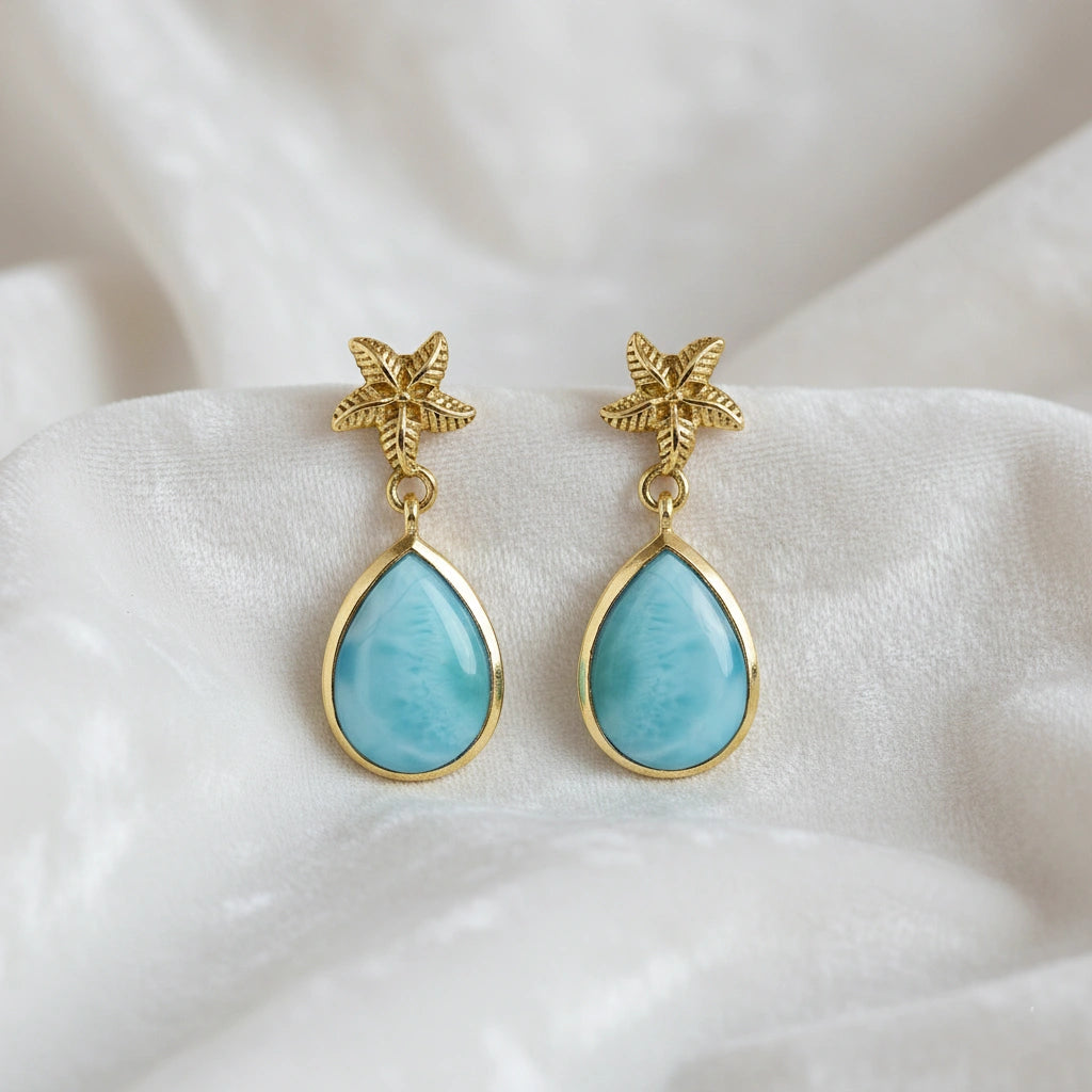 Starfish earrings gold tone larimar teardrop dangle on white draped fabric from a straight angle vie