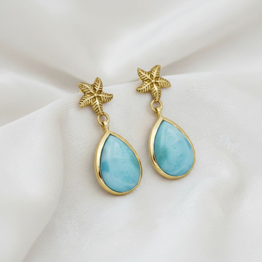 Starfish earrings gold tone larimar teardrop dangles on off white velvet fabric background from a slight angle view