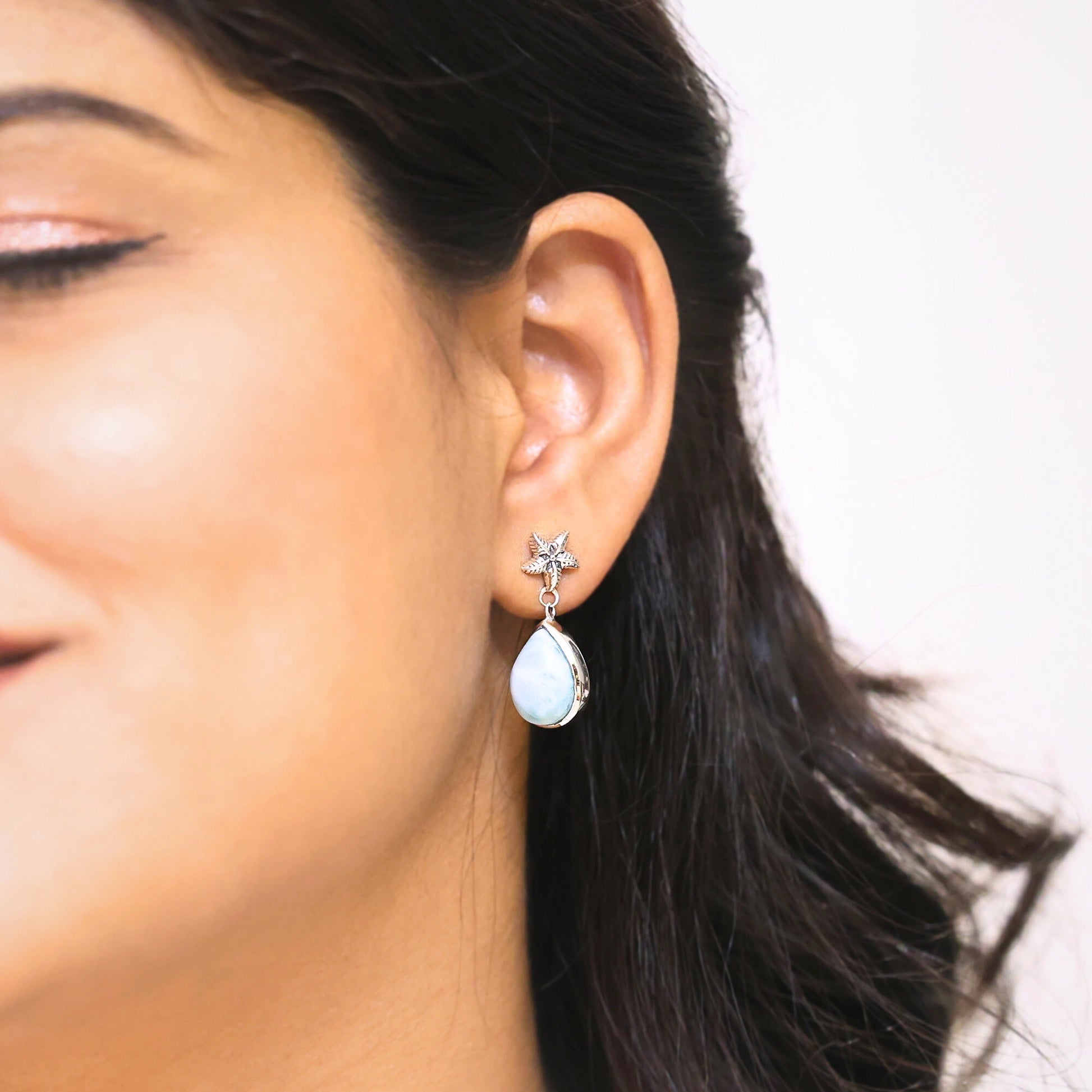 Sterling silver starfish earrings with a larimar teardrop worn by a woman in a side profile on a light background