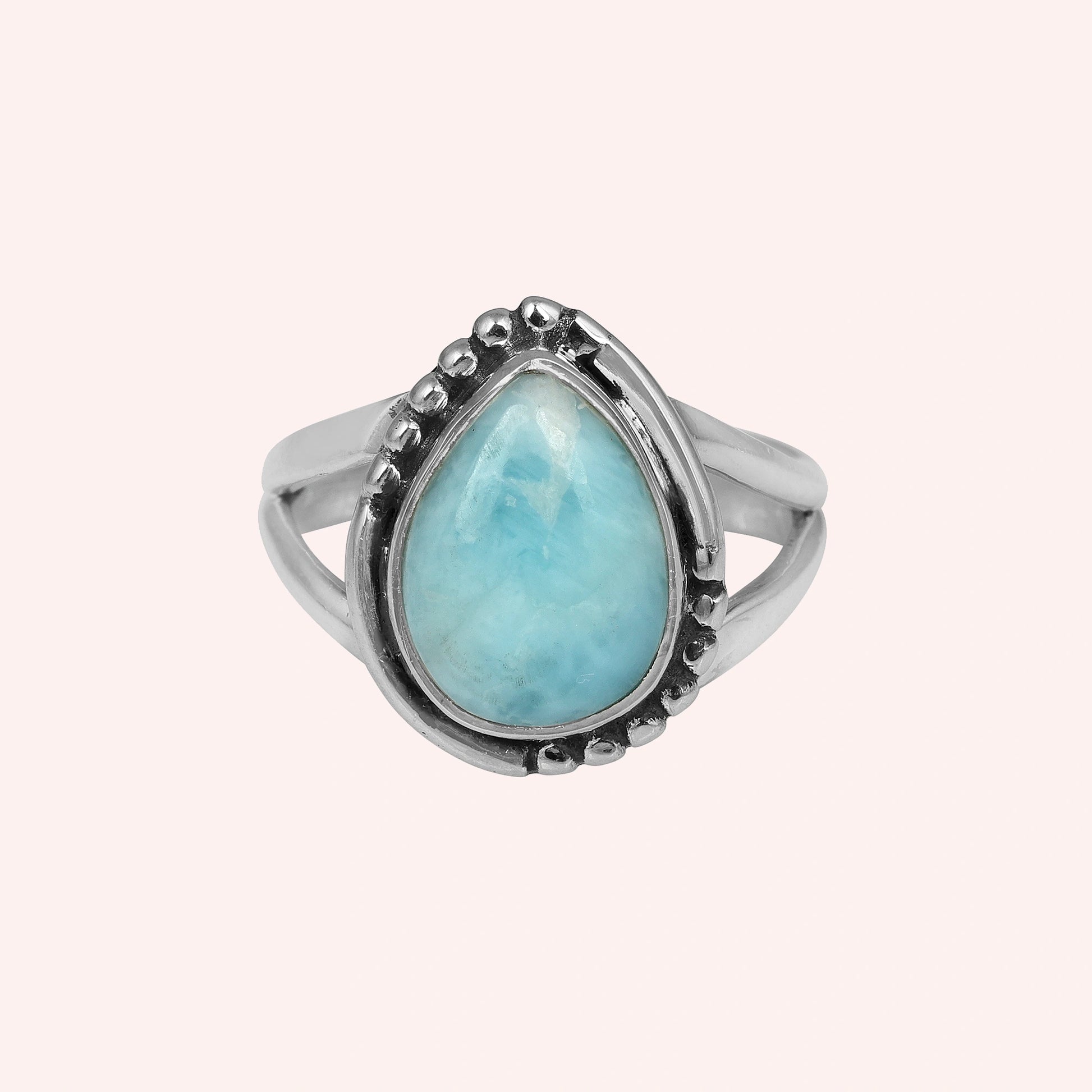 Studio shot of a beautiful silver teardrop ring with a Larimar stone on a light pink solid background viewed straight on