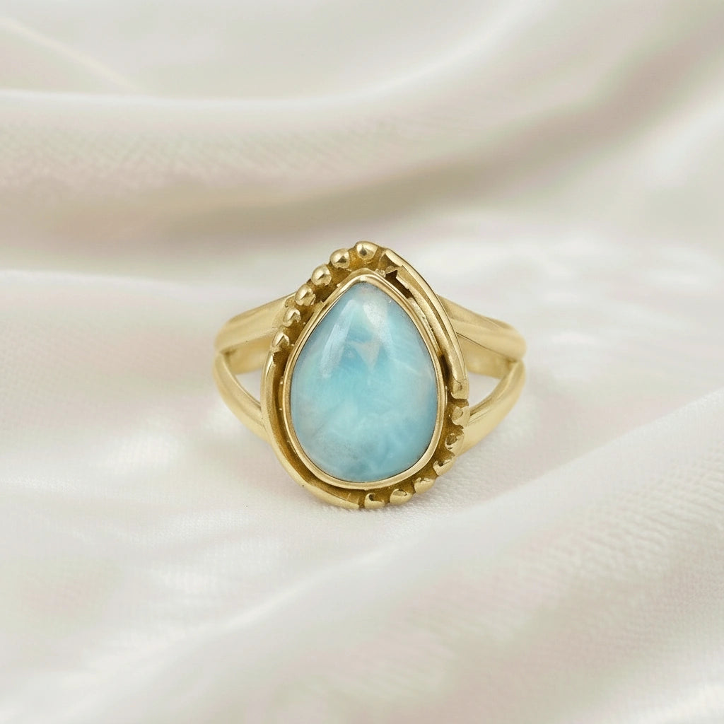 Gold plated silver teardrop ring with teardrop larimar gemstone on light pink background from a straight product angle view