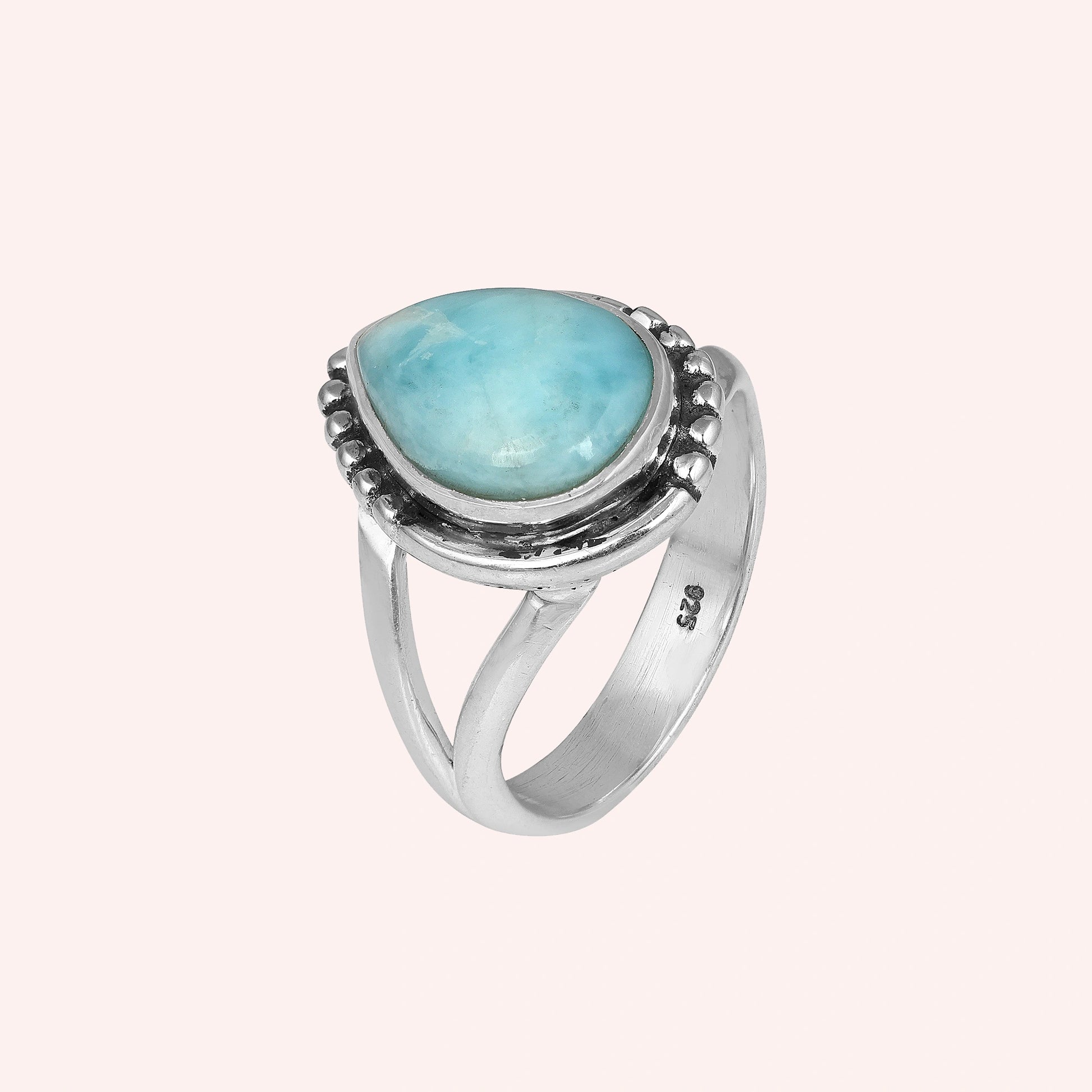 Studio shot of a beautiful silver teardrop ring with a Larimar stone on a pink background viewed from an elevated side angle