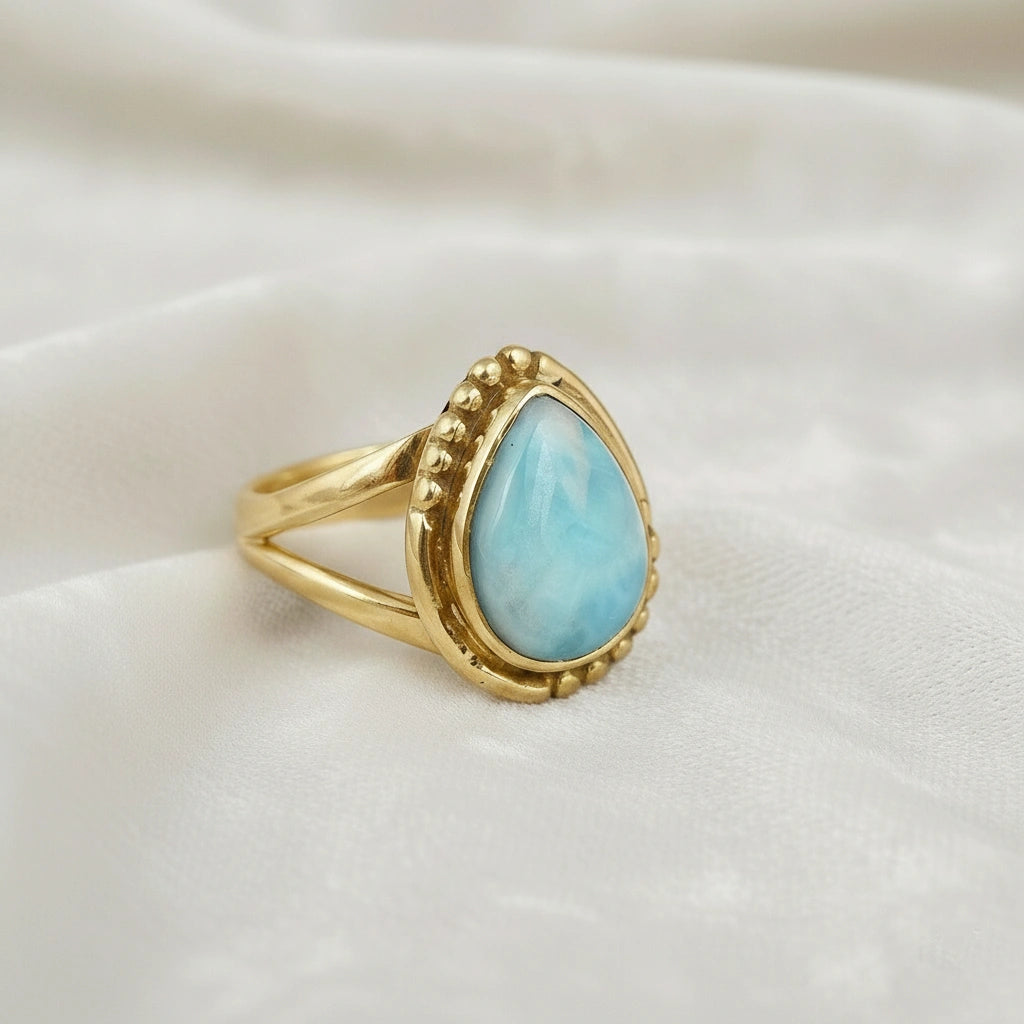 Gold plated silver teardrop ring with teardrop larimar gemstone on light pink background from a slight angle view