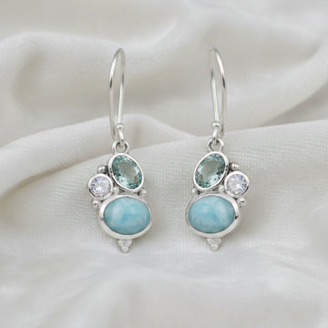 Boho dangle earrings with a sterling silver trio gemstones larimar moonstone blue topaz on white fabric from a straight angle view