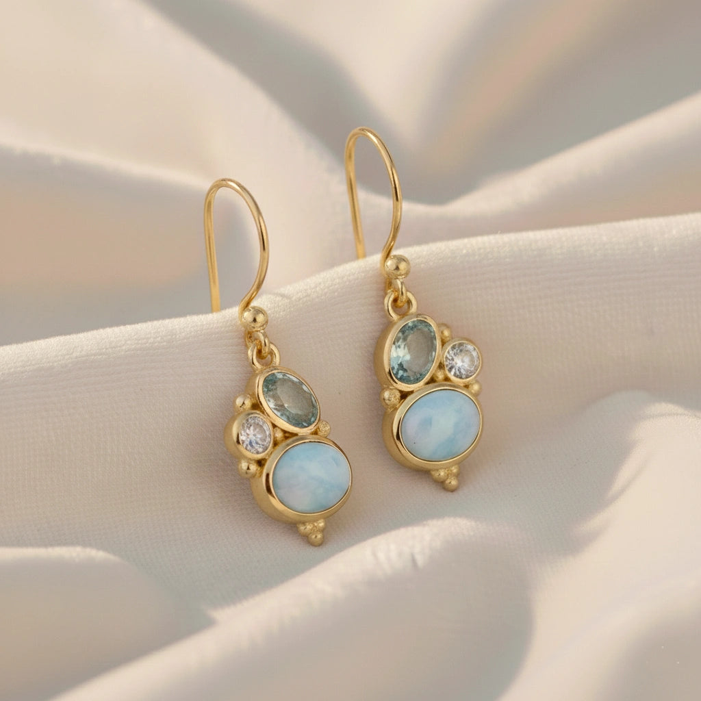 Gold plated boho dangle earrings with a trio gemstones larimar blue topaz moonstone on white draped fabric slight angled view