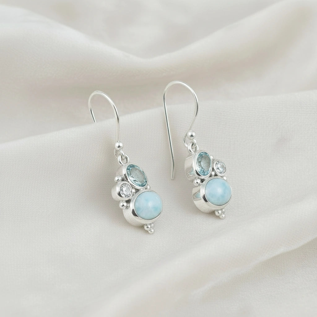 Boho dangle earrings sterling silver trio gemstones larimar moonstone blue topaz on white fabric from an overhead angle view