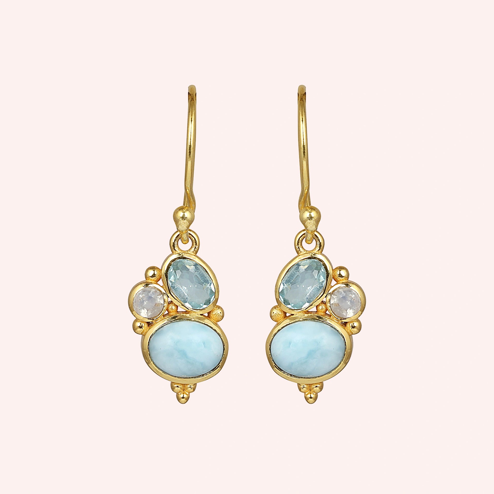 Gold plated boho dangle earrings with a trio of gemstones larimar blue topaz moonstone on light pink background front angle view