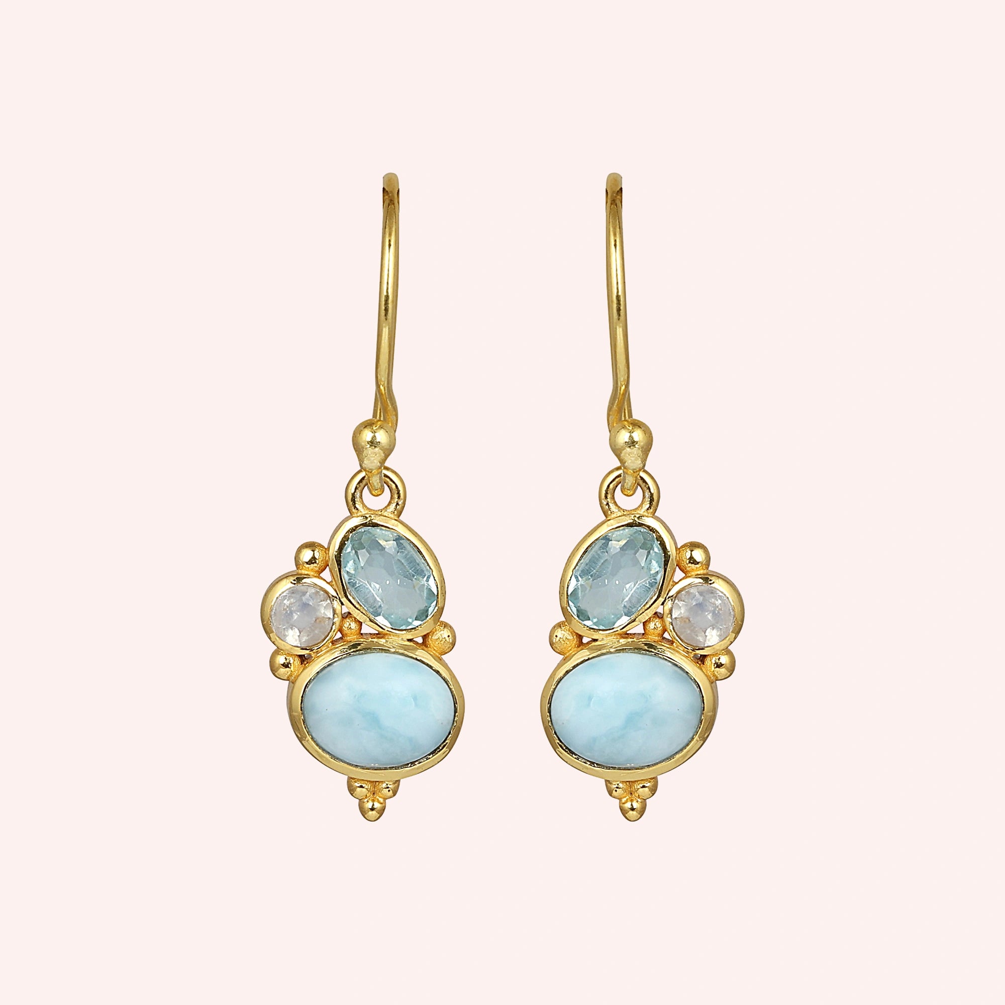 Gold plated boho dangle earrings with a trio of gemstones larimar blue topaz moonstone on light pink background front angle view