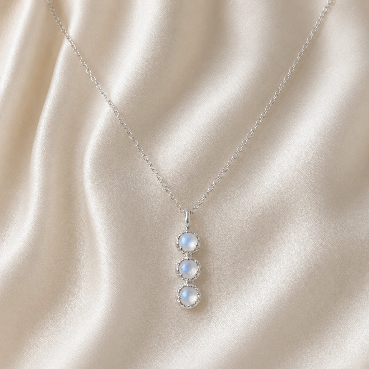 Layering_necklace_in_sterling_silver_at_front_angle_featuring_moonstone_drop_on_a_soft_fabric_background
