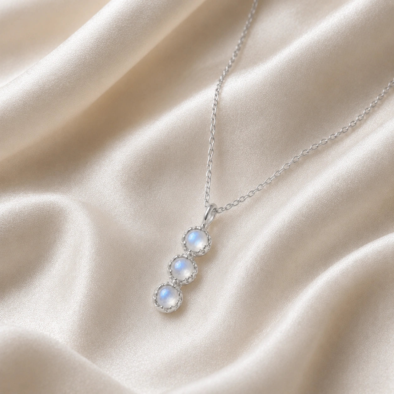 Layering_necklace_in_sterling_silver_at_slight_angle_featuring_moonstone_drop_on_a_soft_fabric_background