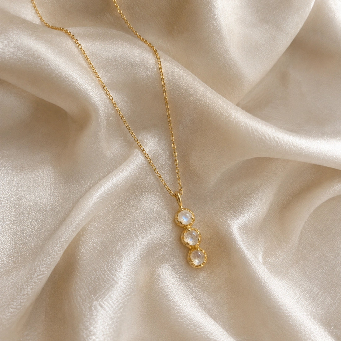Layering_necklace_in_gold_plated_silver_at_slight_angle_featuring_moonstone_drop_on_a_soft_fabric_background