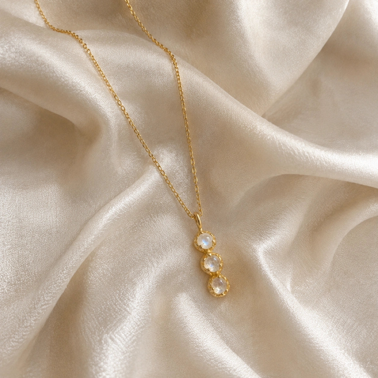 Layering_necklace_in_gold_plated_silver_at_slight_angle_featuring_moonstone_drop_on_a_soft_fabric_background