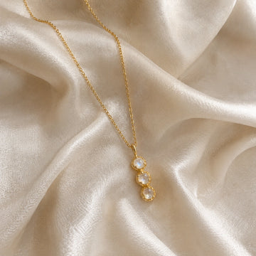 Layering_necklace_in_gold_plated_silver_at_slight_angle_featuring_moonstone_drop_on_a_soft_fabric_background