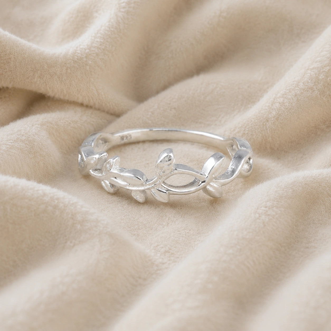 Leaf_ring_in_sterling_silver_with_a_floral_design_at_front_angle_on_soft_fabric_background