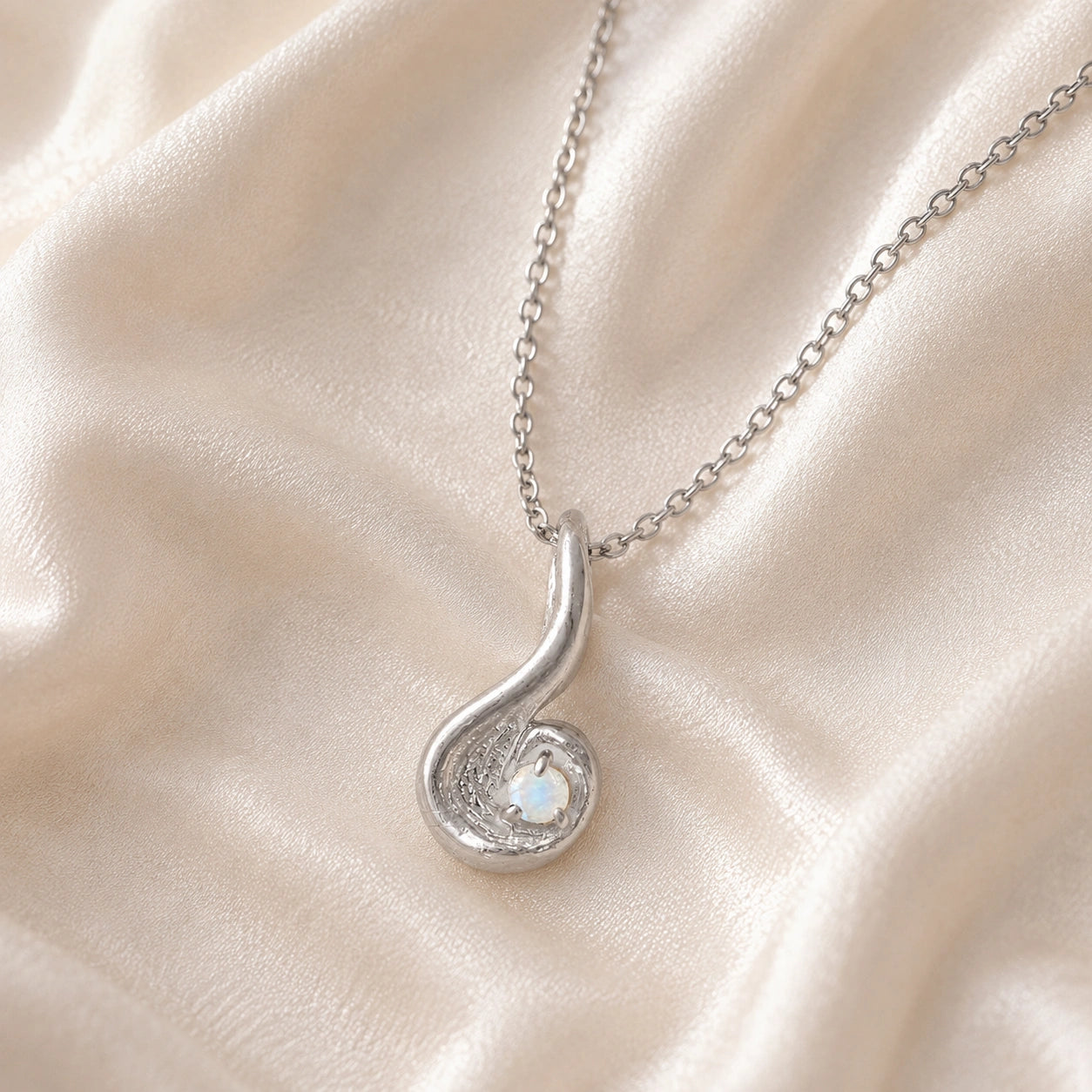 Locket_necklace_with_sterling_silver_teardrop_pendant_and_moonstone_at_front_angle_on_soft_fabric_background
