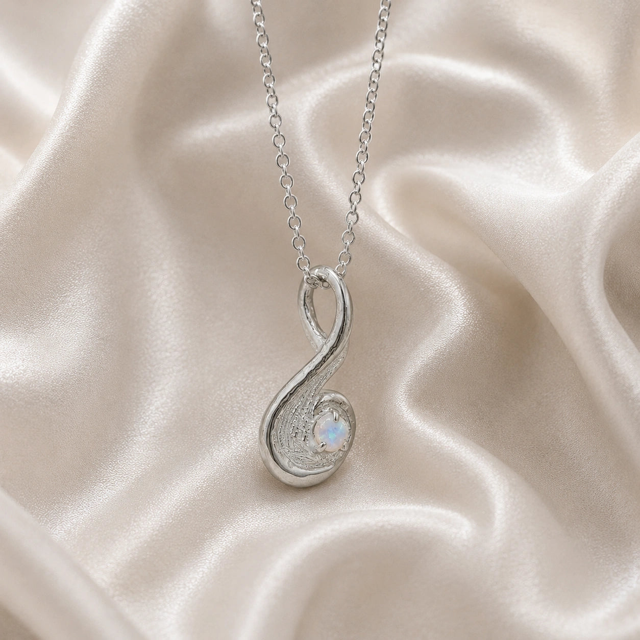 Locket_necklace_with_sterling_silver_teardrop_pendant_and_moonstone_at_slightly_angled_on_soft_fabric_background
