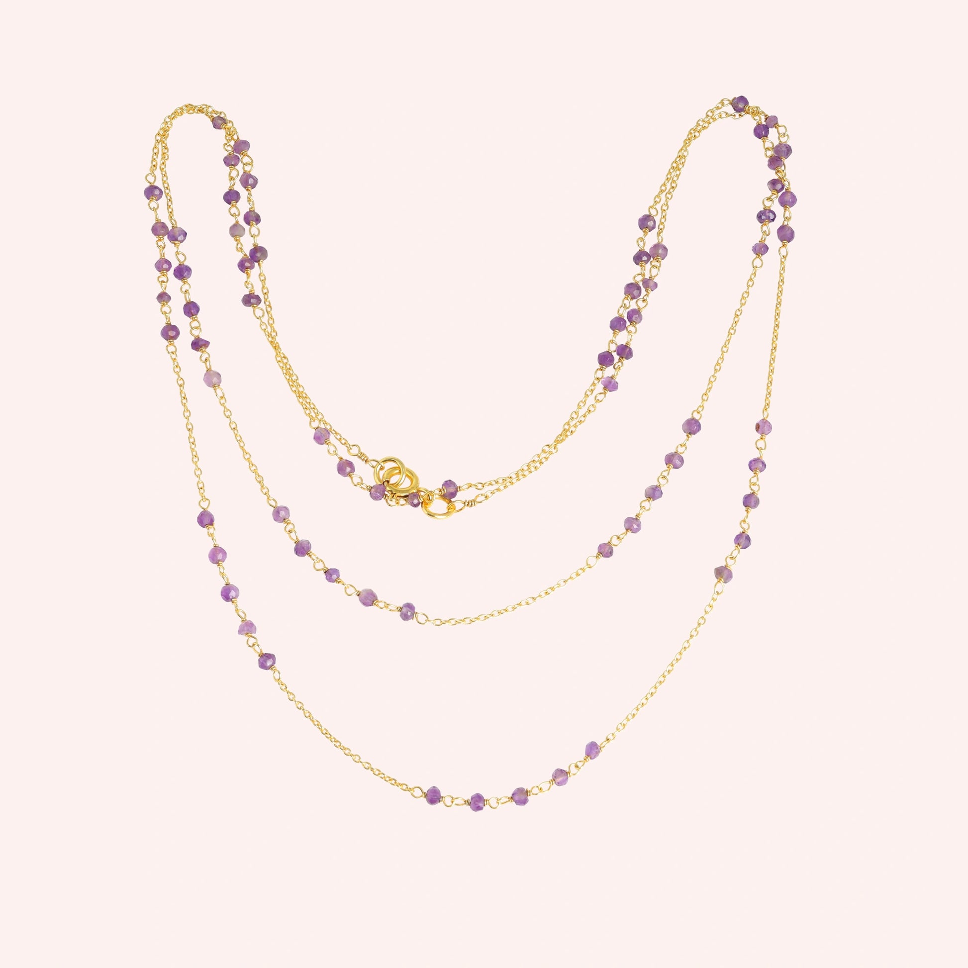 Long_chain_necklace_in_gold_plated_silver_with_amethyst_beads_at_front_angle_view_on_solid_pink_background