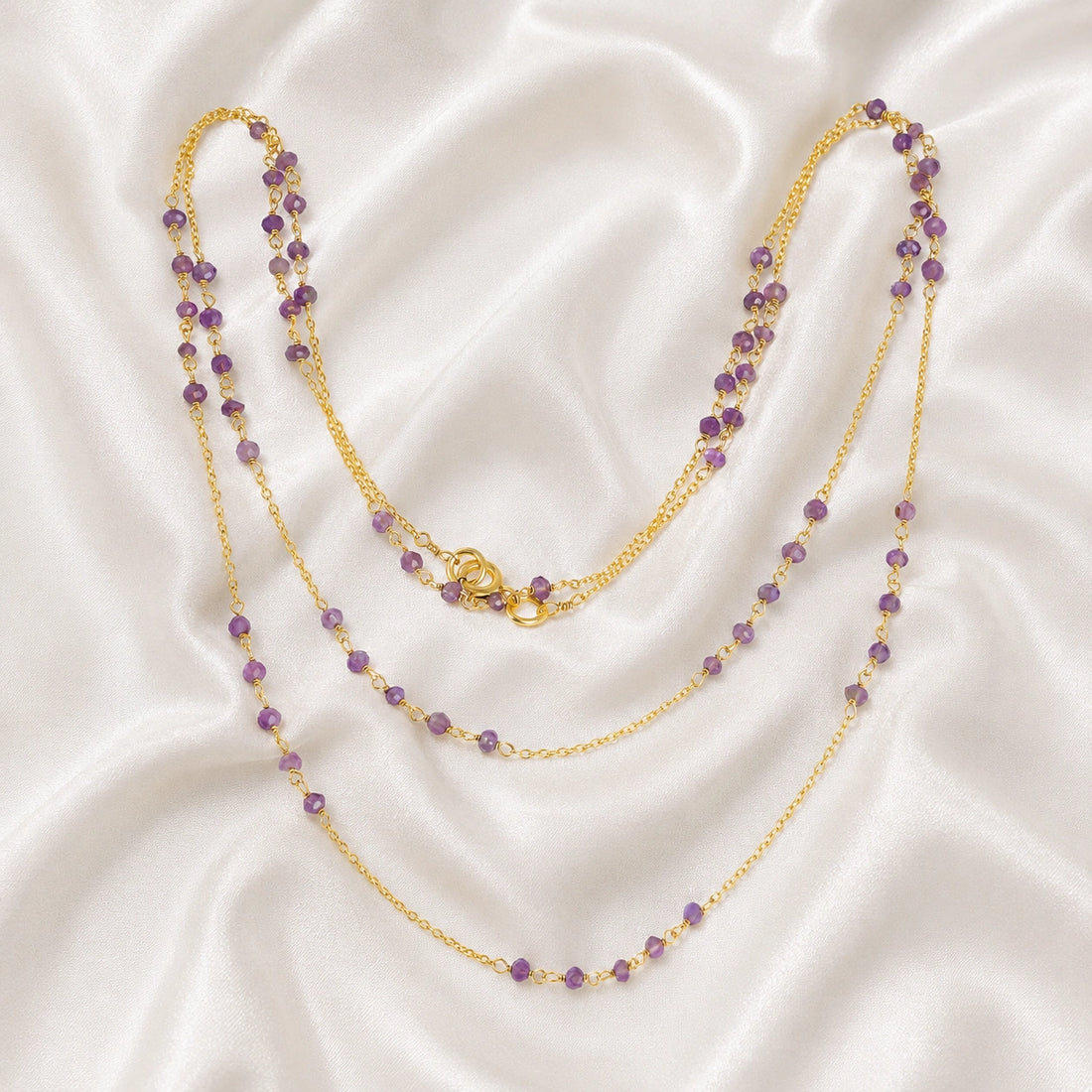 Long_chain_necklace_in_gold_plated_silver_with_amethyst_beads_at_front_angle_view_on_soft_fabric_background