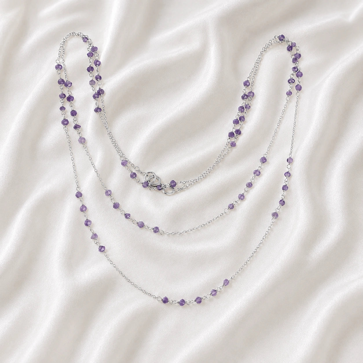 Long_chain_necklace_in_sterling_silver_with_amethyst_beads_at_front_angle_view_on_soft_fabric_background