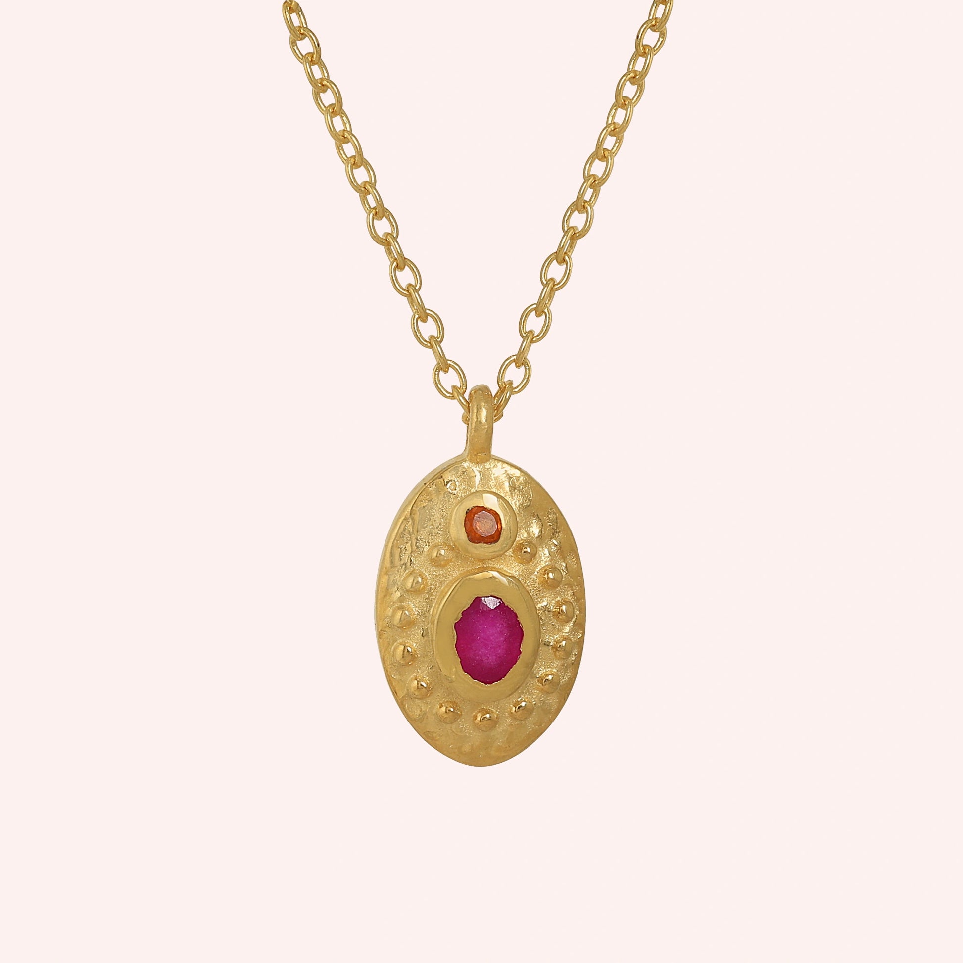 Medallion_necklace_in_gold_plated_silver_front_angle_with_oval_pendant_with_ruby_and_carnelian_stones_on_solid_pink_background