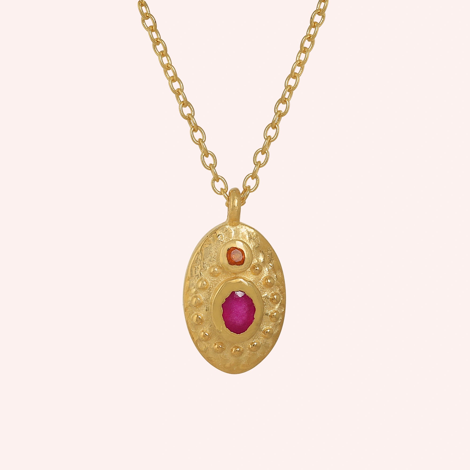 Medallion_necklace_in_gold_plated_silver_front_angle_with_oval_pendant_with_ruby_and_carnelian_stones_on_solid_pink_background