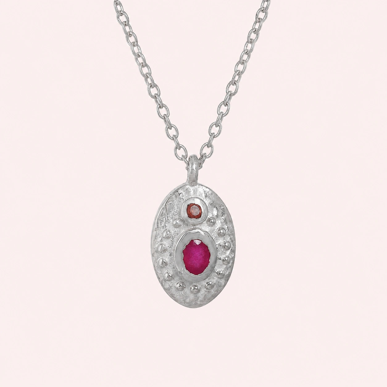 Medallion_necklace_in_sterling_silver_front_angle_with_oval_pendant_with_ruby_and_carnelian_stones_on_solid_pink_background