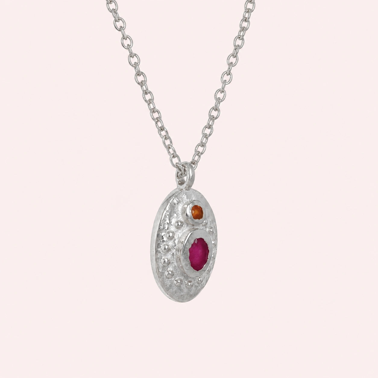Medallion_necklace_in_sterling_silver_slight_angle_with_oval_pendant_with_ruby_and_carnelian_stones_on_solid_pink_background