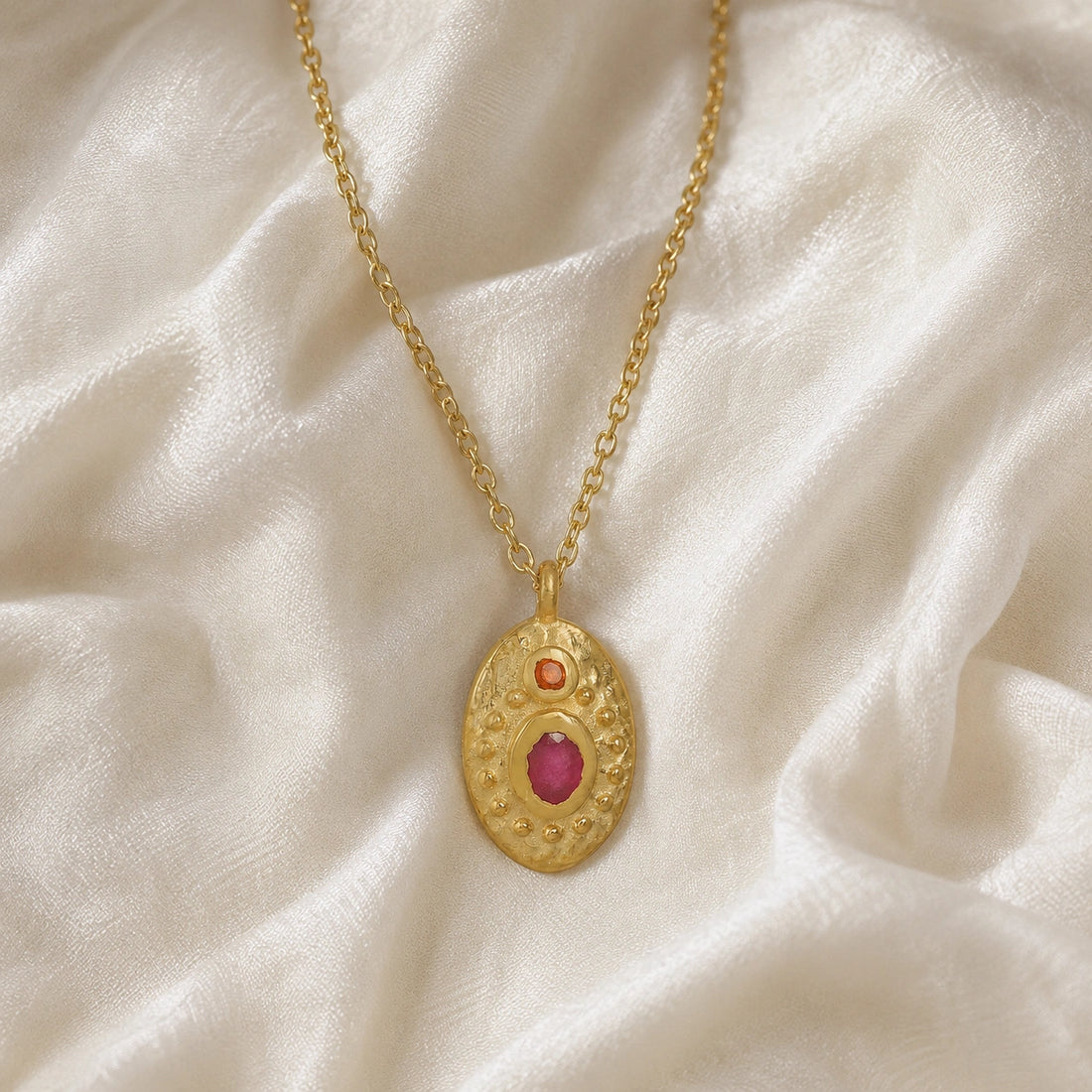 Medallion_necklace_in_gold_plated_silver_front_angle_with_oval_pendant_with_ruby_and_carnelian_stones_on_soft_fabric_background