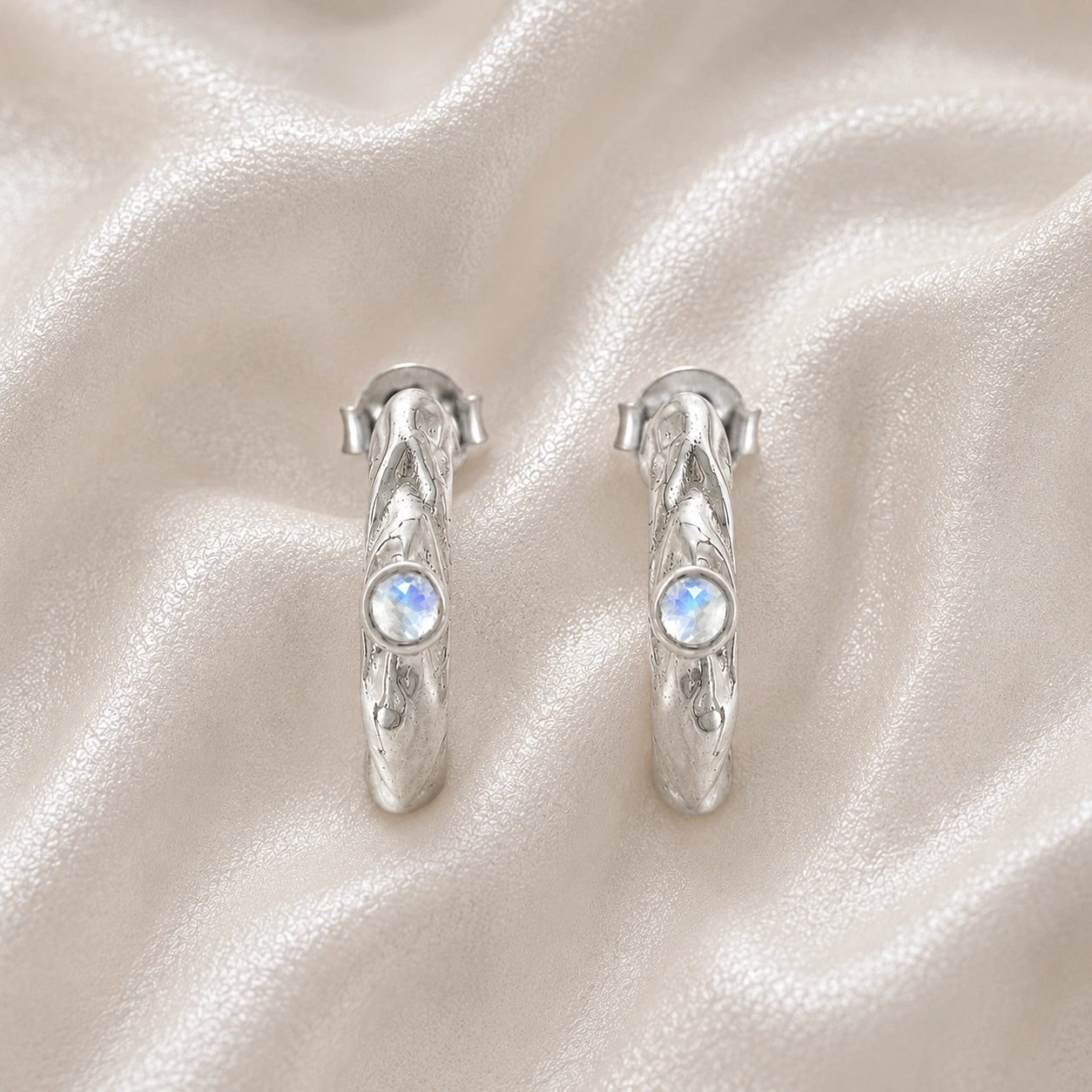 Mini_hoop_earrings_sterling_silver_hoop_design_with_moonstone_in_front_angle_view_on_soft_fabric_background