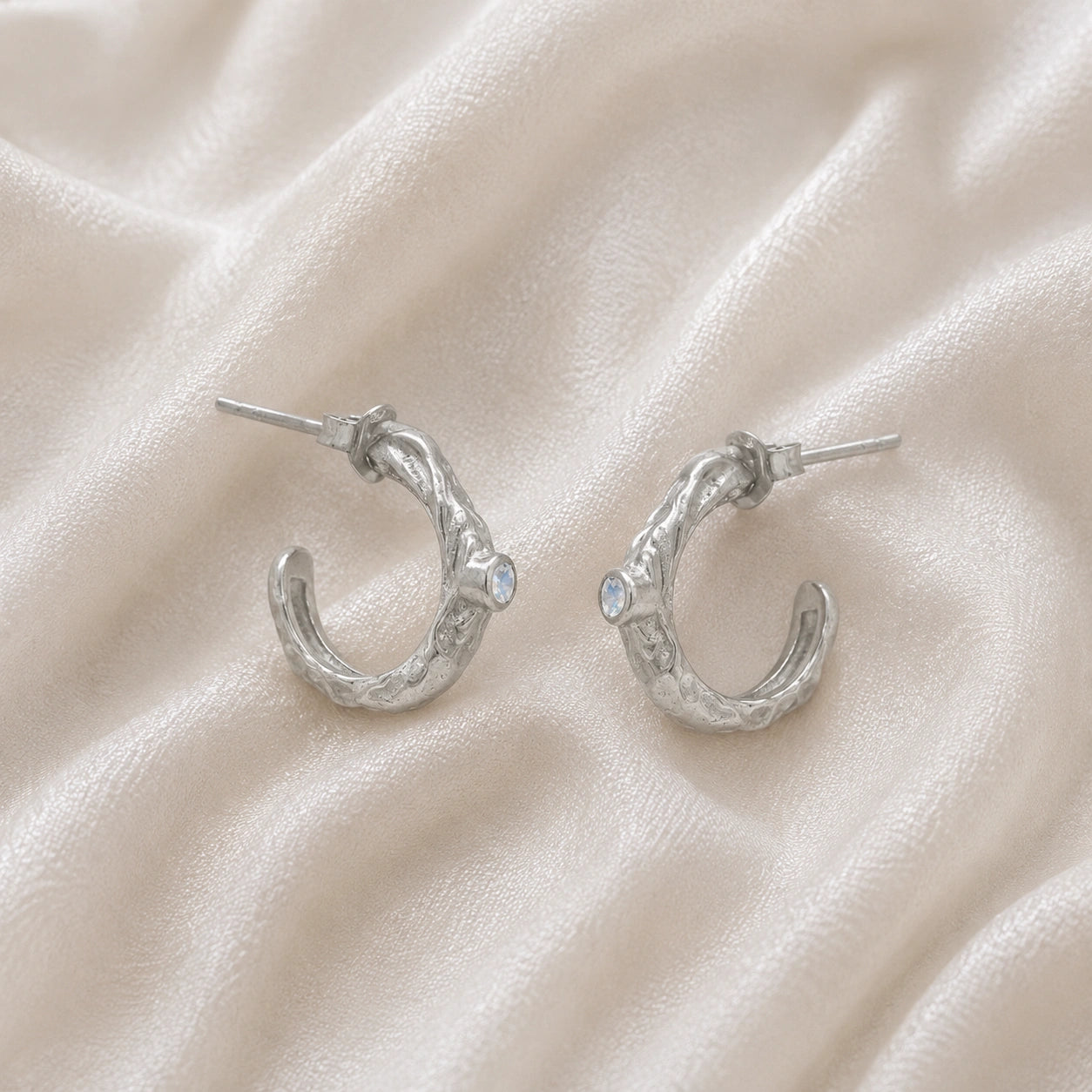 Mini_hoop_earrings_sterling_silver_hoop_design_with_moonstone_in_side_angle_view_on_soft_fabric_background