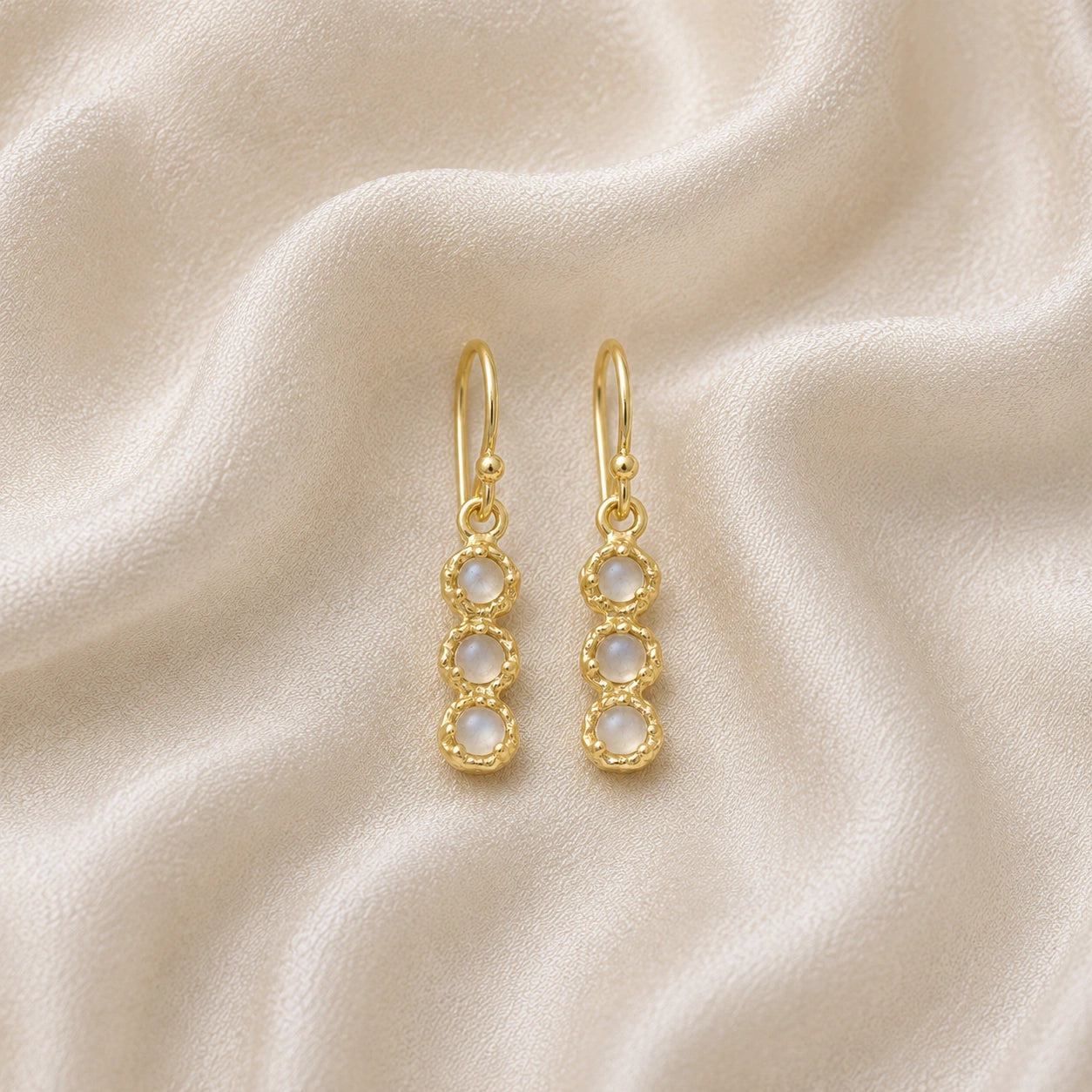 Minimal_earrings_in_gold_plated_silver_at_front_angle_featuring_moonstone_drops_on_a_soft_fabric_background