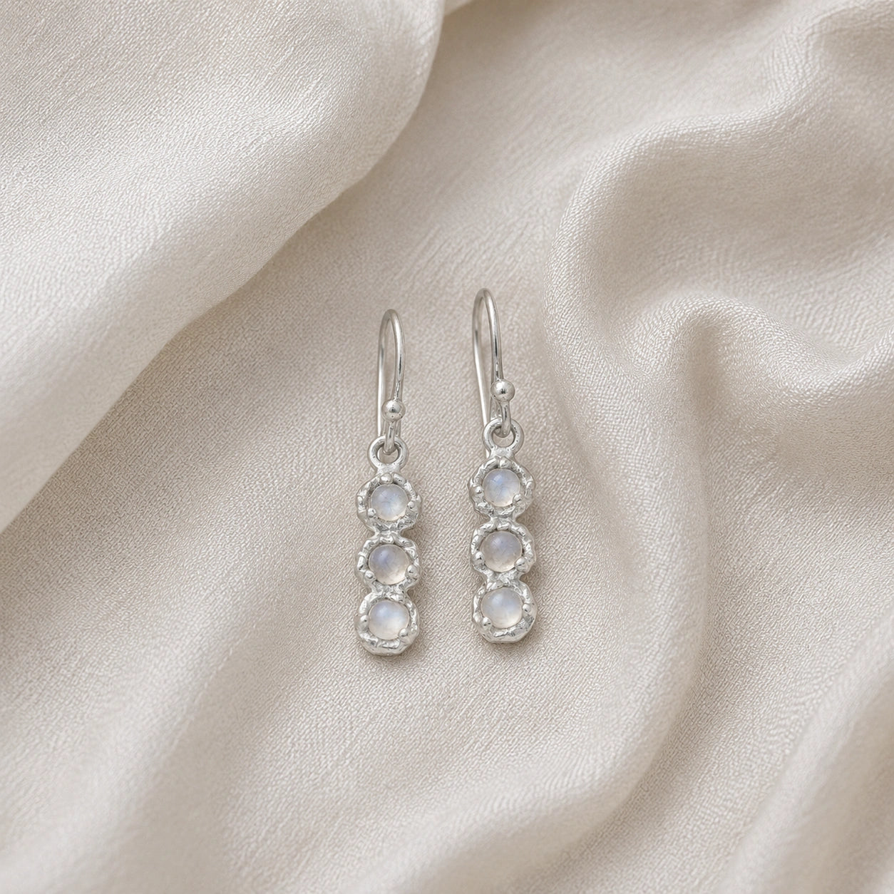Minimal_earrings_in_sterling_silver_at_front_angle_featuring_moonstone_drops_on_a_soft_fabric_background