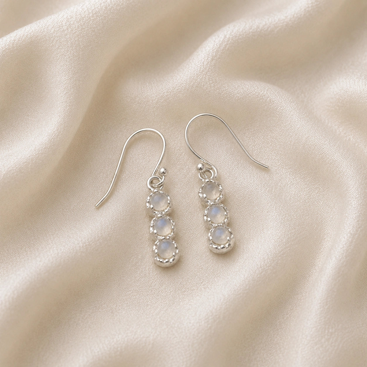 Minimal_earrings_in_sterling_silver_at_slightly_angled_featuring_moonstone_drops_on_a_soft_fabric_background