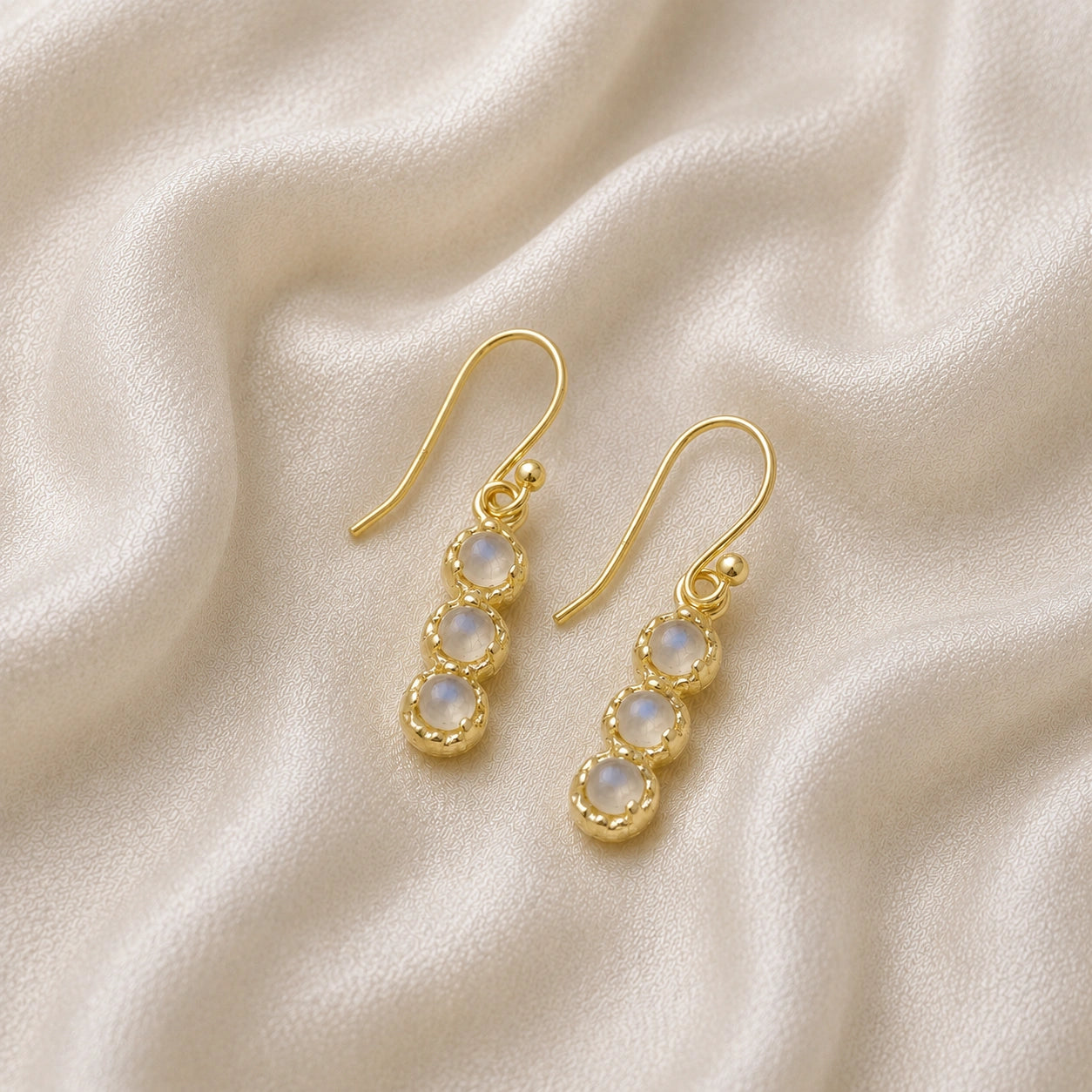 Minimal_earrings_in_gold_plated_silver_at_slightly_angled_featuring_moonstone_drops_on_a_soft_fabric_background