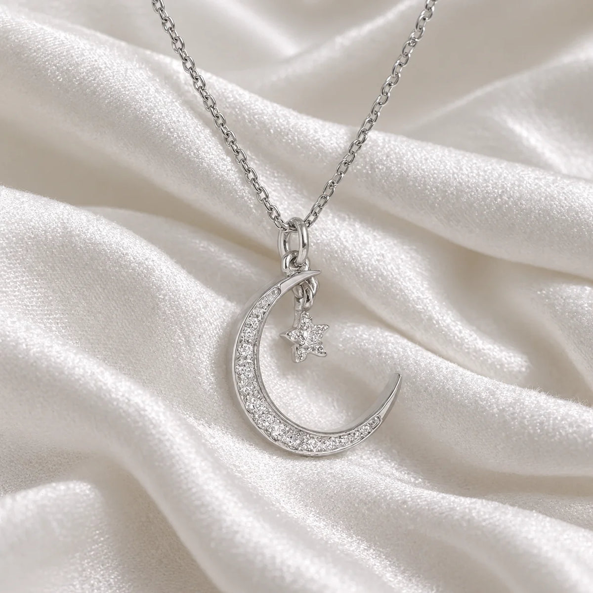 Moon_necklace_in_sterling_silver_with_a_small_star_charm_at_slight_angle_view_on_soft_fabric_background