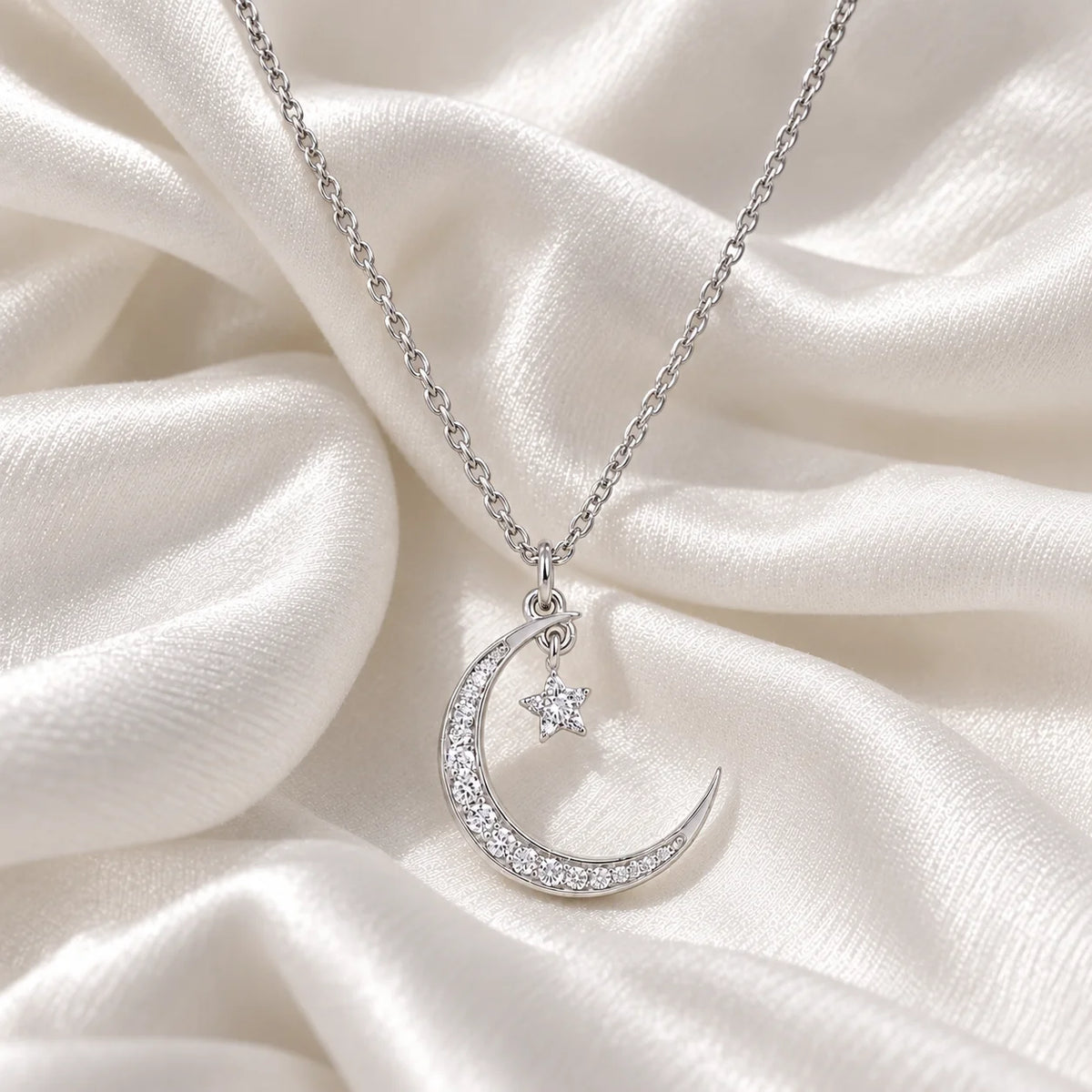 Moon_necklace_in_sterling_silver_with_a_small_star_charm_at_front_angle_view_on_soft_fabric_background